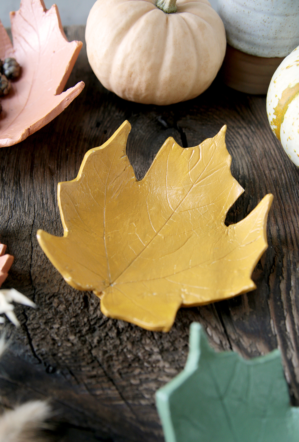 yellow painted clay leaf bowl on wood board with pumpkins and leaf bowls around it